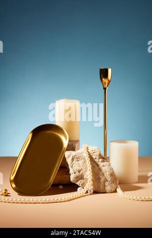 Vorderansicht von zwei weißen Kerzen, die neben einer Steinplatte platziert sind, mit Perlen und Requisiten auf einem pastellbraunen Tisch mit blauem Hintergrund. Szene für adve Stockfoto