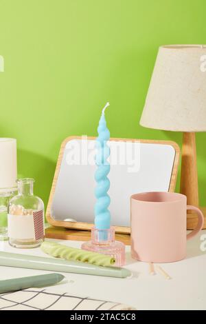 Eine blaue Kerze wird in einen Glaskerzenhalter eingesetzt. Auf dem Tisch befinden sich viele Utensilien wie Spiegel, Keramikbecher, Lampe usw. Suita mit empfindlichen Bildern Stockfoto