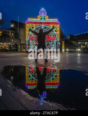 Ein Mann erhebt seine Arme im Sieg durch die Reflexion von We Rise by Heben Anderen von Marinella Senatore auf der Southbank. Stockfoto