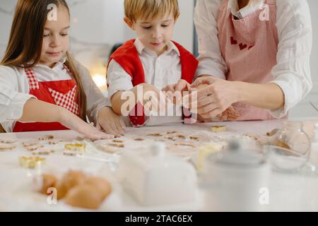 Nahaufnahme von Kinderhänden, die Kekse aus Teig ausschneiden. Ein kleines Mädchen und ein Junge machen Weihnachtskekse. Stockfoto