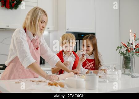 Mutter mit ihren süßen kleinen Kindern macht Weihnachtskekse in der Küche Stockfoto