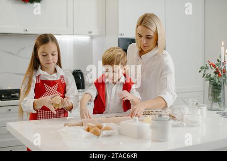 Eine Mutter bringt ihrer Tochter und ihrem kleinen Sohn bei, wie man Kekse macht. Eine Frau und ihre Kinder bereiten Weihnachtskekse mit einer Teigform zu. Stockfoto