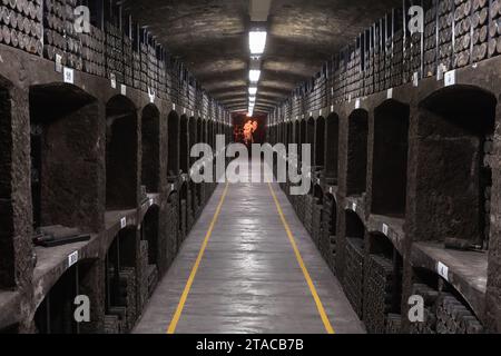 Massandra, Krim - 11. August 2020: Inneres des Weinguts Massandra, perspektivischer Blick auf einen dunklen Korridor mit gestapelten Flaschen Stockfoto