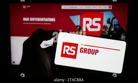 Person, die ein Mobiltelefon mit dem Logo der britischen Stromverteilerfirma RS Group plc vor der Unternehmenswebseite hält. Schwerpunkt auf dem Display des Telefons. Stockfoto