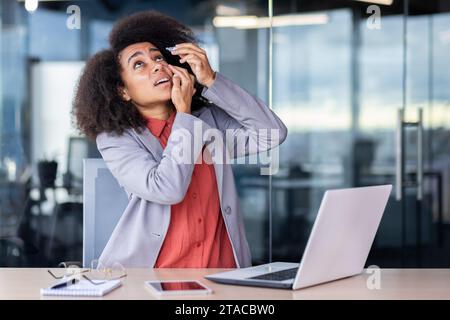 Geschäftsfrau tropft Augentropfen, Geschäftsfrau, die lange Zeit mit dem Laptop arbeitet, überarbeitet und müde am Arbeitsplatz im Büro, Angestellte im Business-Anzug und lockiges Haar. Stockfoto