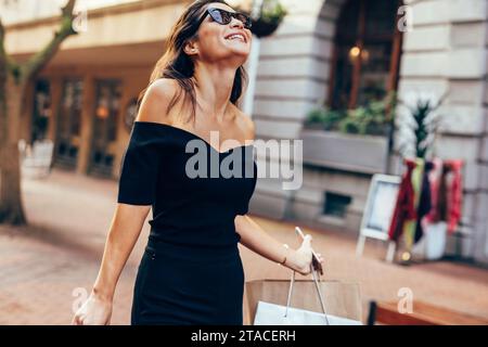 Asiatische Frau mit Einkaufstüten auf Straße der Stadt. Weibliche Walking im Freien mit Tüten und lächelnd. Stockfoto