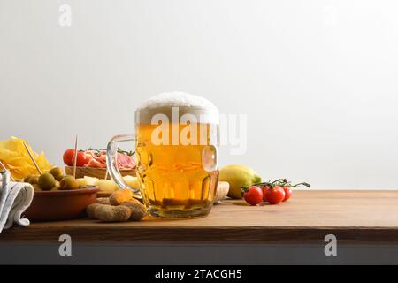 Bierbecher auf einer Holzbank und Snacks auf einem weißen, isolierten Hintergrund. Vorderansicht. Stockfoto