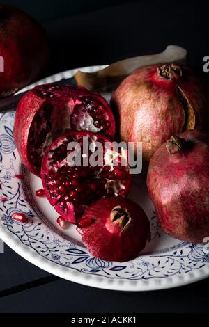 Frische Granatäpfel auf alten rustikalen Tisch Stillleben in dunklen Tönen. Reife und saftige Granatapfelfrüchte in Nahaufnahme auf schwarzem Hintergrund. Stockfoto