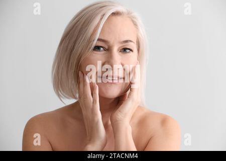 Reife Frau geben sich Massage auf hellen Hintergrund Gesicht Stockfoto