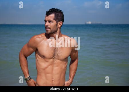 Junger, gutaussehender muskulöser Mann, der im blauen Wasser steht und wegschaut. Stockfoto