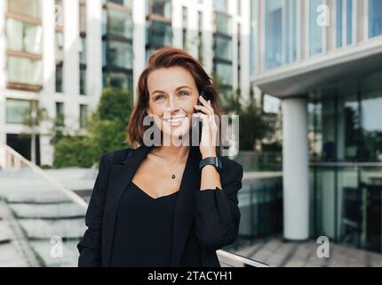 Porträt einer lächelnden Frau mittleren Alters in formeller Kleidung, die im Freien telefoniert Stockfoto