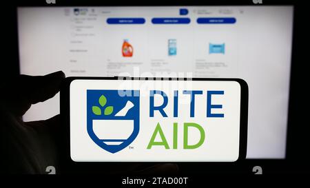 Person, die ein Mobiltelefon mit dem Logo der amerikanischen Drogerie-Firma Rite Aid Corporation vor der Webseite hält. Schwerpunkt auf dem Display des Telefons. Stockfoto