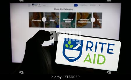 Person, die ein Handy mit dem Logo der US-Drogeriemarkt-Firma Rite Aid Corporation vor der Webseite hält. Schwerpunkt auf dem Display des Telefons. Stockfoto