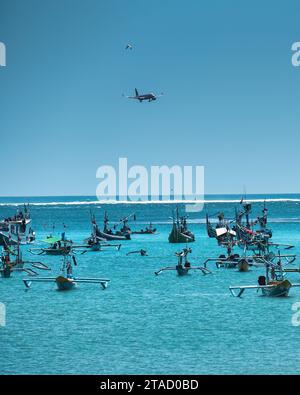 Flugzeug und Vogel fliegen über Jukung traditionelles Boot im tropischen Meer auf Bali, Indonesien Stockfoto