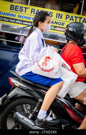 Ein thailändisches Schulmädchen sitzt hinten in einem Motorradtaxi, das durch die geschäftigen Straßen von Pattaya City, Bangkok, fährt. Stockfoto