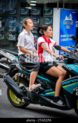 Ein thailändisches Schulmädchen sitzt hinten in einem Motorradtaxi, das durch die geschäftigen Straßen von Pattaya City, Bangkok, fährt. Stockfoto