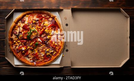 Paprika-Pizza mit Paprika, Zuckermais und Rucola in offener Schachtel auf dunklem Holztisch flach liegend mit Kopierraum Stockfoto