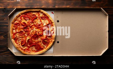 Paprika-Pizza mit Paprika in offener Kartonbox auf dunklem Holztisch flach liegend mit Kopierraum Stockfoto