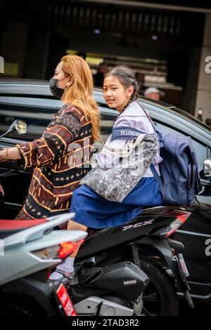 Ein thailändisches Schulmädchen sitzt hinten in einem Motorradtaxi, das durch die geschäftigen Straßen von Pattaya City, Bangkok, fährt. Stockfoto