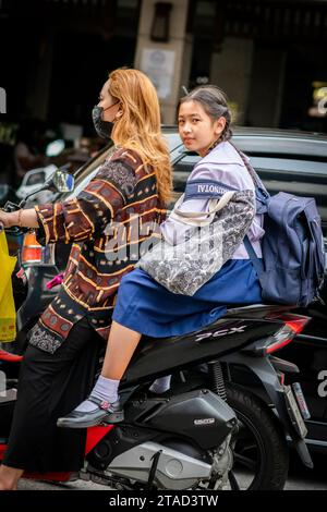 Ein thailändisches Schulmädchen sitzt hinten in einem Motorradtaxi, das durch die geschäftigen Straßen von Pattaya City, Bangkok, fährt. Stockfoto