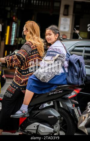 Ein thailändisches Schulmädchen sitzt hinten in einem Motorradtaxi, das durch die geschäftigen Straßen von Pattaya City, Bangkok, fährt. Stockfoto