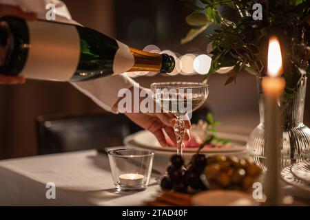 Champagner wird von der Flasche zum Glas auf dem Tisch gegossen Stockfoto