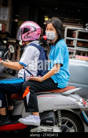 Ein thailändisches Schulmädchen sitzt hinten in einem Motorradtaxi, das durch die geschäftigen Straßen von Pattaya City, Bangkok, fährt. Stockfoto