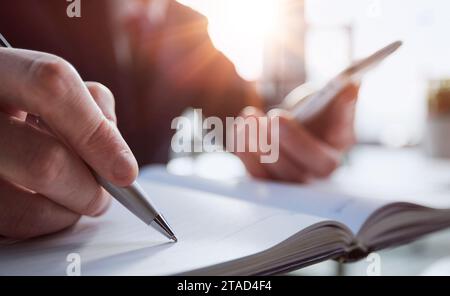 In der Nähe von Frau Hände in Spirale Notepad schreiben auf Holz- Desktop mit verschiedenen Gegenständen platziert Stockfoto