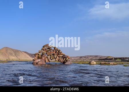 Ein Felsvorsprung in einem Fluss in der Nähe eines Steinhaufens, der zusammengestapelt ist Stockfoto