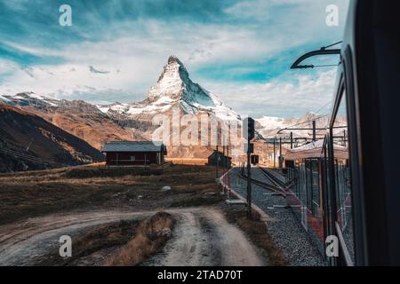 Atemberaubender Blick auf das Matterhorn mit Zug, der an sonnigen Tagen auf Riffelboden in Zermatt, Schweiz, zum Bahnhof Gornergrat fährt Stockfoto