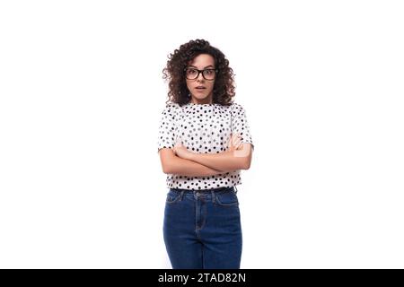 Süße, lockige junge Brünette mit schulterlangem Haar, die eine Sommerbluse trägt, trägt eine Brille Stockfoto