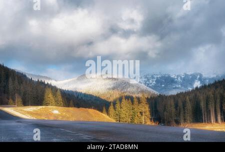Wunderschöne Winterlandschaft mit schneebedeckten Bergen, Bäumen, Straßen und bewölktem Himmel Stockfoto