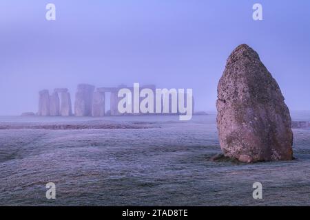 Der Heel Stone und Stonehenge bei Sonnenaufgang an einem nebeligen, frostigen Morgen, Wiltshire, England. Winter (Januar) 2022. Stockfoto