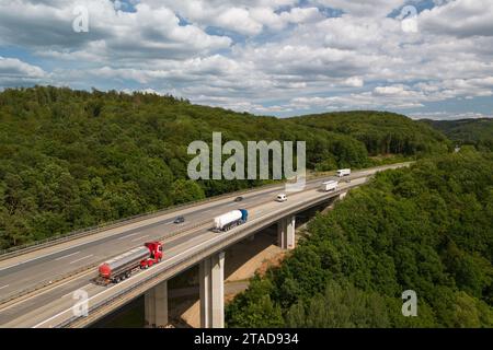 Mehrere Nutzfahrzeuge fahren auf einer stark befahrenen Autobahn durch ein üppiges, bewaldetes Tal Stockfoto