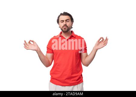 Ein junger, ruhiger europäischer Brünette mit Bart in einem roten T-Shirt meditiert Stockfoto