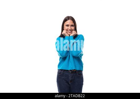 Junge angenehm überraschte hübsche europäische Brünette Frau in einem blauen Button-Down-Pullover freut sich auf einem weißen Hintergrund mit Kopierraum Stockfoto