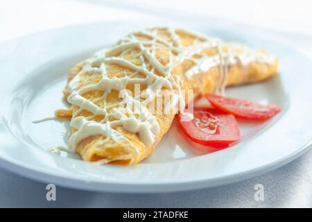 Gerollte Eieromelette gefüllt mit Hühnchen, garniert mit Mayonnaise und Tomaten Stockfoto