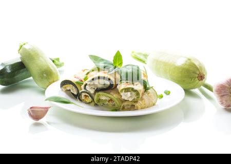 Gekochte Zucchinirollen mit Käse im Inneren, auf einem Teller isoliert auf weißem Hintergrund Stockfoto