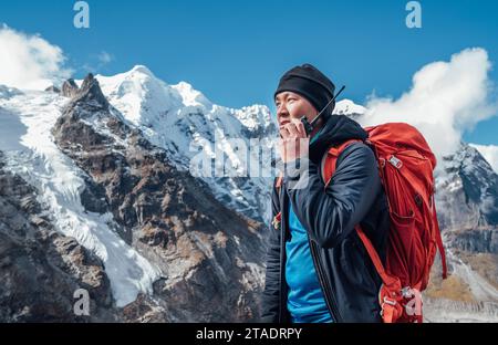 Porträt eines Sherpa-Mannes mit Rucksack, der Walkie-Talkie benutzt, um einen Rettungshubschrauber mit Mera Peak 6476 m Hintergrund zu rufen. Expedition im hohen Himalaya DURIN Stockfoto