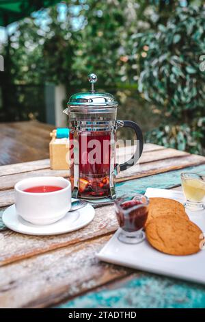 Glas Teekanne Tee und Kekse auf einem Holztisch draußen. Stockfoto