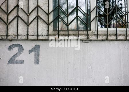 Hausnummerierung. Die Nummer 21 21 21 ist mit einer Schablone auf eine graue Wand unter einem Fenster mit Gittern gemalt Stockfoto