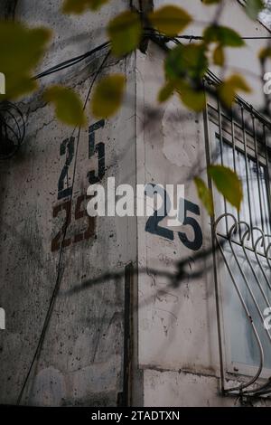 Hausnummer 25. Die Zahl fünfundzwanzig ist dreimal mit einer Schablone auf eine graue Wand an der Ecke des Hauses gemalt, nahe Fenster mit Gittern Stockfoto