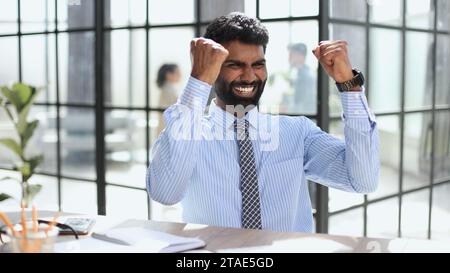 Ein glücklicher Geschäftsmann, der einen Anzug trägt und den Erfolg bei der Arbeit im Büro feiert Stockfoto