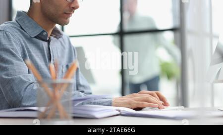 Seitenansicht eines selbstbewussten, bärtigen, konzentrierten Geschäftsmanns, der am Tisch sitzt und mit dem Laptop arbeitet Stockfoto