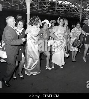 1960er Jahre, historisch, Hochzeitsspaß..., aufgeregte Gäste, geführt von den beiden Brautjungfern, schließen sich unter den Bögen des Bahnhofs Vauxhall an, um der Braut- und Bräutigam-off-Kamera auf einem Zugwagen zu geben - ein großer Abstecher für die Flitterwochen, England, Großbritannien. Stockfoto