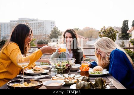 Glückliche Freunde essen veganes Essen und haben Spaß im Restaurant im Freien. Multirassische Menschen genießen gemeinsam Diner Stockfoto