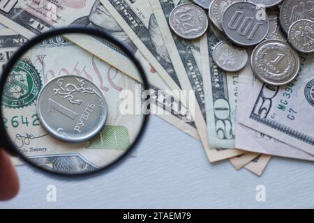 Zahlungsverzug in Russland und Stärkung des Rubels. Ein russischer Rubel unter einer Lupe, vor dem Hintergrund von Dollarscheine und verschiedenen Münzen Stockfoto