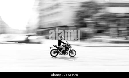 Ein erwachsener Mann, der einen Helm trägt und mit einem Motorrad fährt, fährt durch eine Kreuzung auf einer Stadtstraße Stockfoto