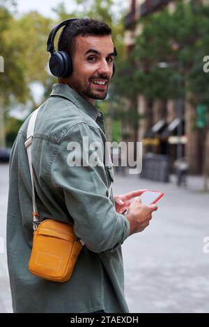 Porträt eines jungen Mannes, der draußen auf der Straße läuft, Musik hört und sich der Kamera zuwendet. Stockfoto