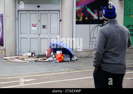 London, Großbritannien. November 2023 30. Ein Mann schaut sich das Eigentum eines Obdachlosen an, der auf dem Bürgersteig in London schläft. Notunterkünfte werden für Londons raue Schläfer eingerichtet, da der Bürgermeister von London in den kommenden Tagen das Unwetterprotokoll in London bei eisigem Wetter implementiert hat. (Foto: Steve Taylor/SOPA Images/SIPA USA) Credit: SIPA USA/Alamy Live News Stockfoto